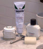Proraso shave set up on a bathroom counter featuring Proraso Sensitive Pre-Shave Cream, Proraso Sensitive Shaving Cream Tube, Proraso Sensitive After Shave Balm, Proraso Post-Shave Stone and a safety razor.