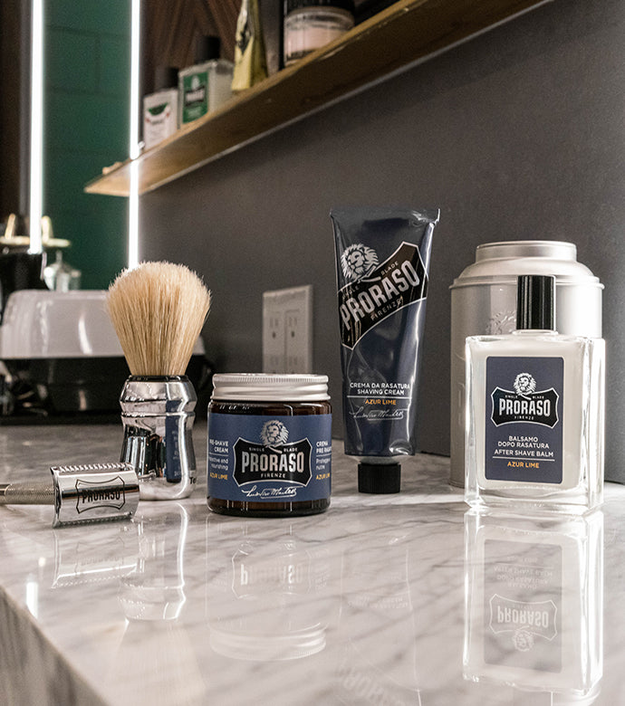 Proraso Single Blade Shave Azur Lime Collection custom razor, Professional Shave Brush, Pre-Shave Cream, Shave Cream Tube and After Shave Balm on the counter of a barber shop.