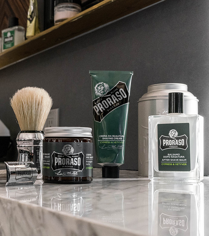 Proraso custom razor, Professional Shave Brush and Single Blade in Cypress & Vetyver collection : Pre-Shave Cream, Shave Cream Tube and After Shave Lotion on a barber shop counter.